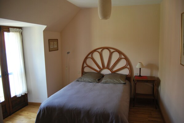 A bedroom with a bed, a bedside table with a lamp, a window with curtains, and a wall-mounted picture. - Appartement Spacieux, Calme. Quercy (Assier)