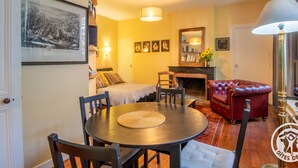 A cozy living room with a round dining table, a red leather sofa, and a fireplace. There are framed pictures on the wall and a lamp on a side table. - Historic Centre Apartment Near Château and Cathedral (Angers)