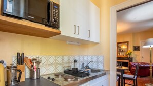 A modern kitchen with white cabinets, a microwave, a stove, and a sink. There is a dining area with a red leather couch and a lamp. - Historic Centre Apartment Near Château and Cathedral (Angers)
