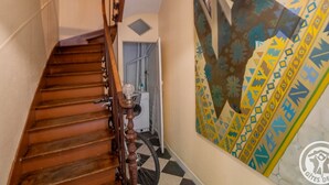A wooden staircase with a handrail, a wall-mounted light fixture, and a colorful abstract painting. - Historic Centre Apartment Near Château and Cathedral (Angers)