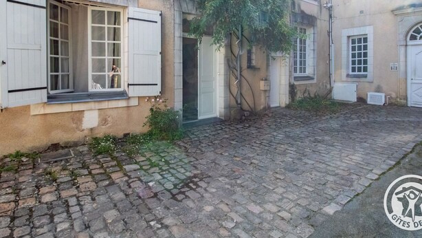 A courtyard with cobblestone paving, a building with white shutters, and a tree with yellow flowers. - Historic Centre Apartment Near Château and Cathedral (Angers)