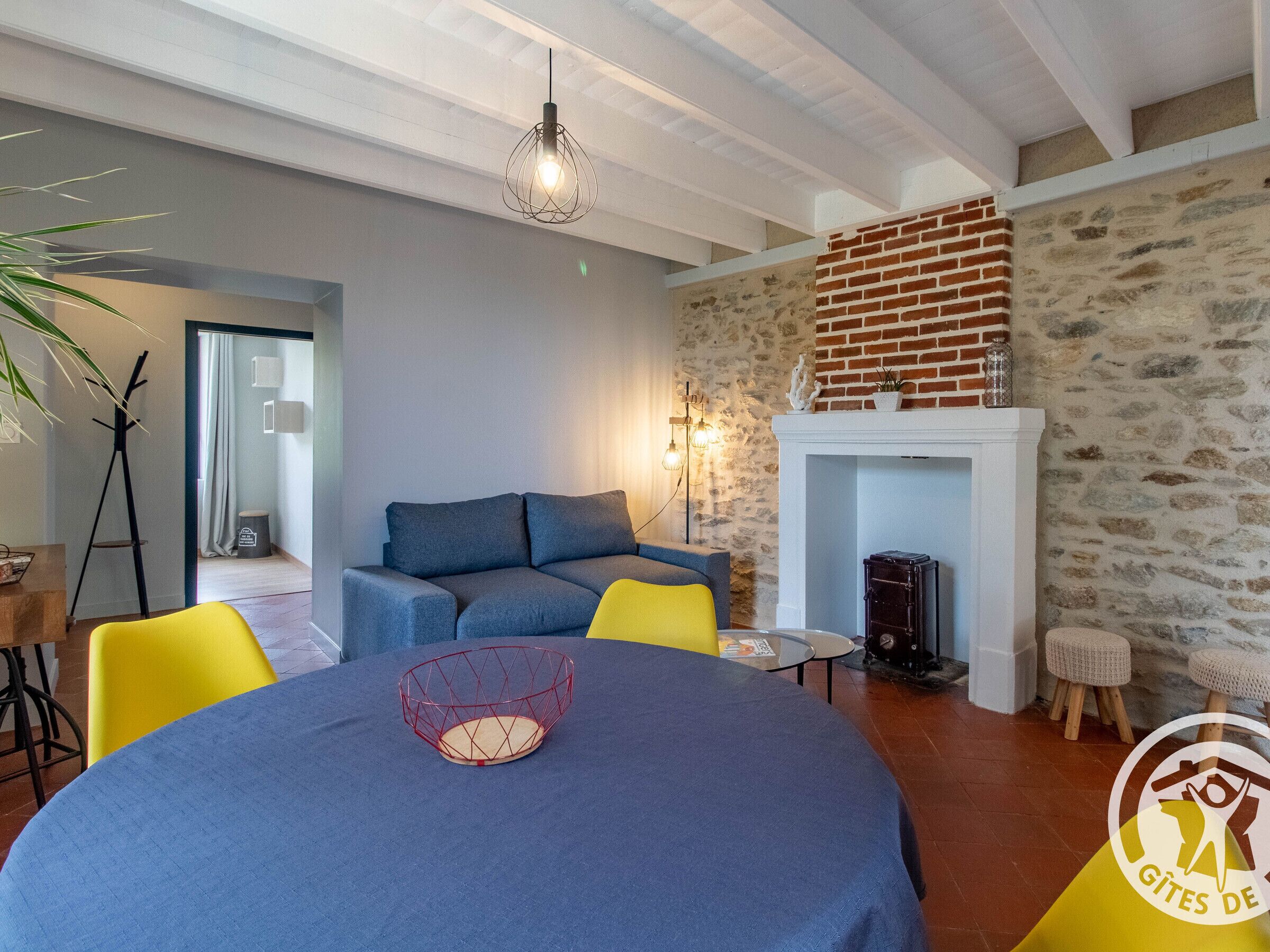A cozy living room with a fireplace, a sofa, a dining table with chairs, and a modern pendant light.