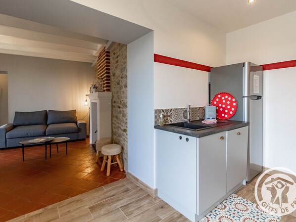 A compact living space with a kitchenette, a grey sofa, a small table, and a patterned rug.