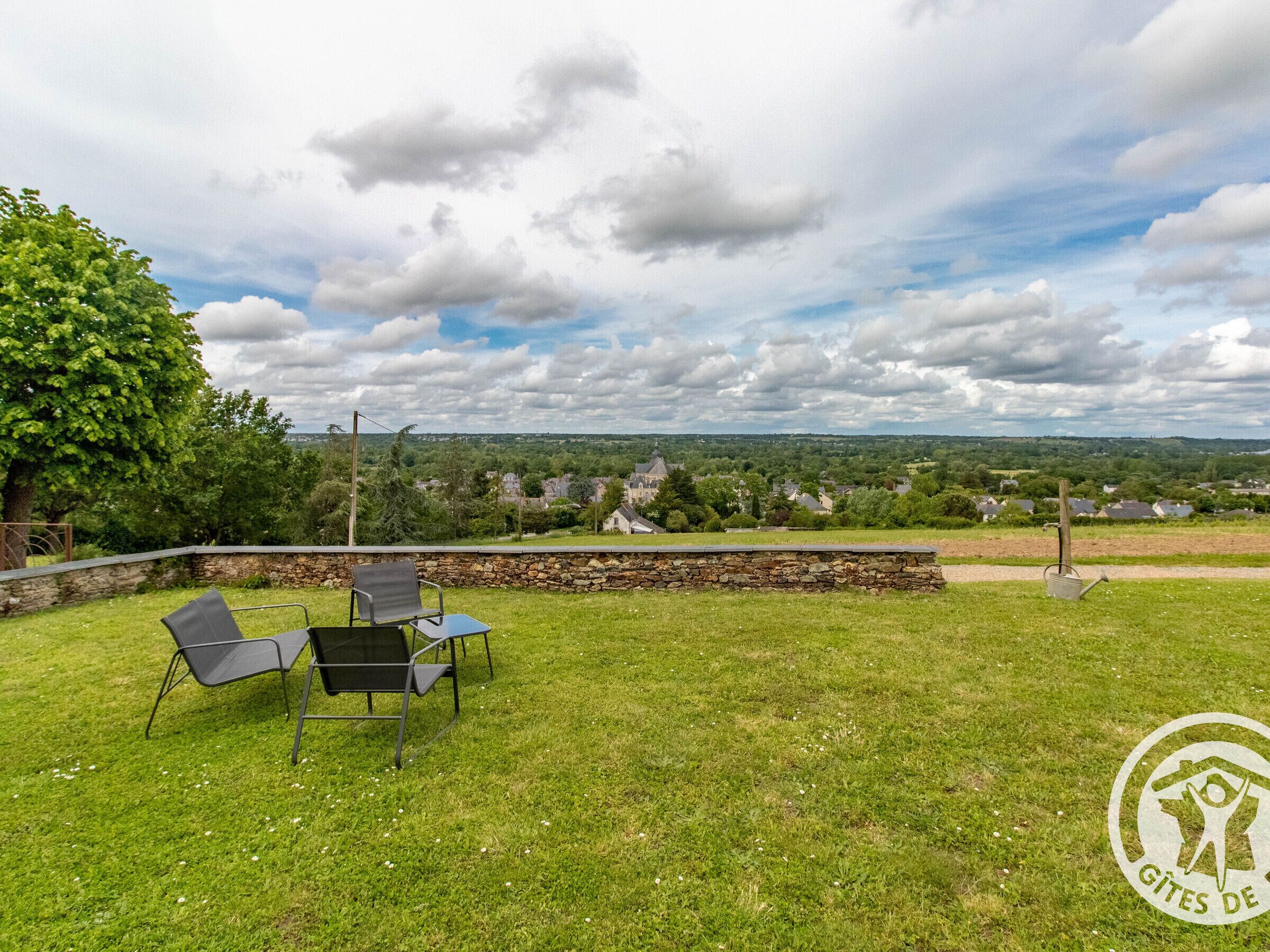 Ruohikkoalue ulkona, jossa on kivimuuri, kaksi tuolia ja näkymä kaupunkiin kauempana.