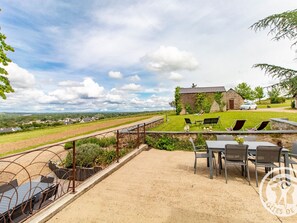 A patio with outdoor seating, a view of a vineyard, and a stone building in the background.