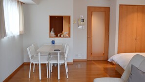 Una habitación de hotel con suelo de madera, una cama, un escritorio con sillas, un espejo y una puerta.