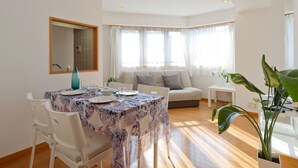 Un comedor con una mesa dispuesta para cuatro, un sofá y un amplio ventanal con cortinas.