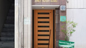 Entrada de un edificio con puerta de madera, una escalera a la izquierda y un letrero que indica 'Annex Higashi-Azabu' y 'Daily-Condo Tokyo Azabu'.