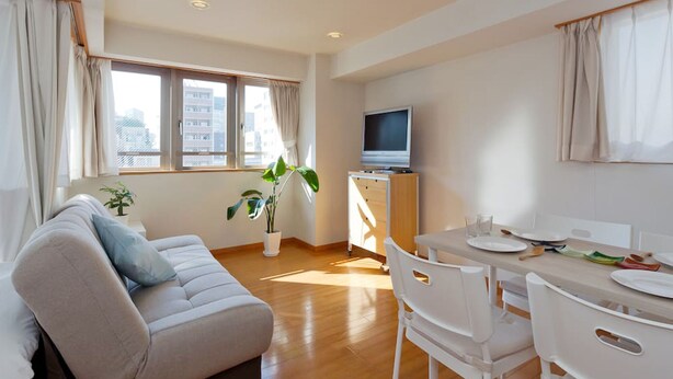 Una sala moderna con sofá, mesa de comedor, sillas, televisor y planta.