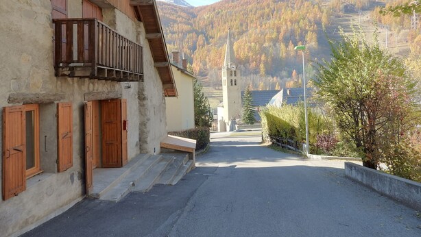 A narrow street with a building featuring wooden shutters and a balcony. A church with a steeple is visible in the distance. - 200 m FROM SKI SLOPES- HOUSE  FOR 12 PERSONS (Chantemerle)