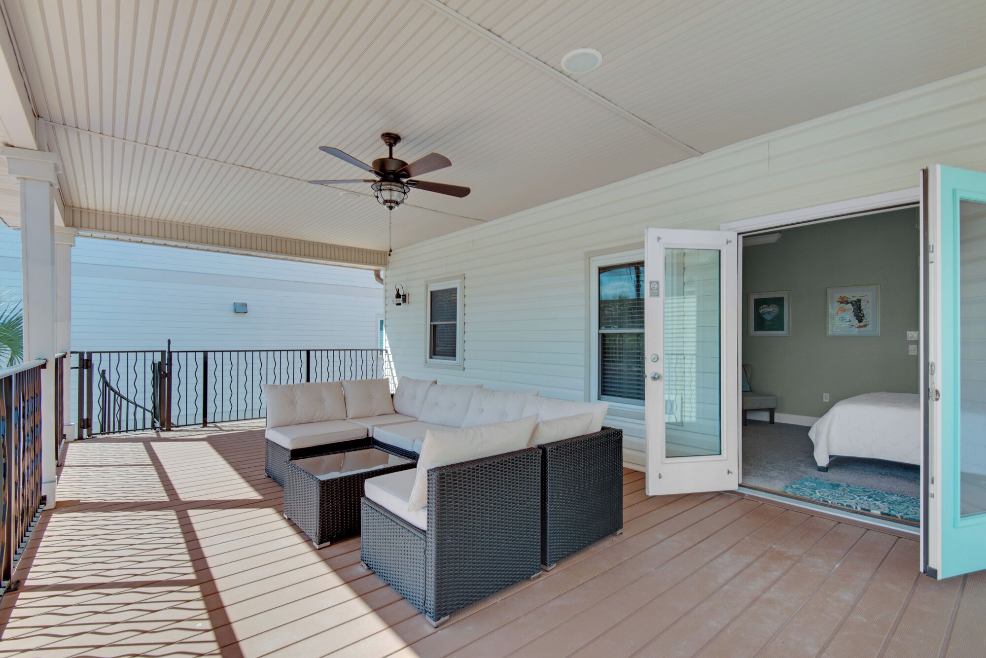A covered outdoor area with a ceiling fan, a wicker sofa, and a door leading to a bedroom.