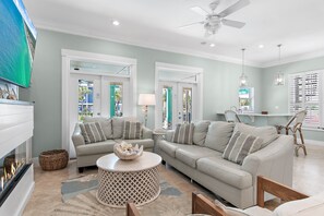 A living room with a fireplace, two sofas, a coffee table, wicker baskets, and a ceiling fan. - ☀Private Fenced in Pool~3 Masters~Remodel~Walk 2 Beach~5BR Seahaus Destin (Destin)