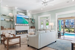 A living room with a fireplace, a large TV, a pool view, and a ceiling fan. - ☀Private Fenced in Pool~3 Masters~Remodel~Walk 2 Beach~5BR Seahaus Destin (Destin)