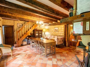 A rustic interior with a wooden staircase, a dining area with a table and chairs, a sofa, and a fireplace.