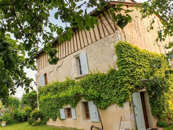 A two-story building with a stone facade, ivy-covered walls, and multiple windows with shutters.