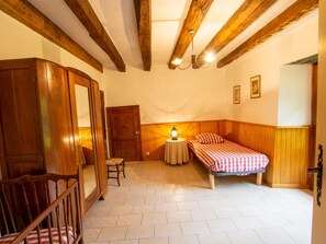 A room with a wooden wardrobe, a bed with checkered bedding, a small table with a lamp, and exposed wooden beams on the ceiling. - Secluded countryside house with 4 bedrooms in Eymet (Eymet)