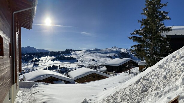 A snow-covered mountain village with wooden buildings and a clear view of the surrounding snowy landscape.