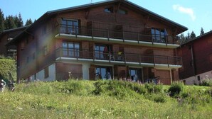 A two-story wooden building with balconies, surrounded by greenery.