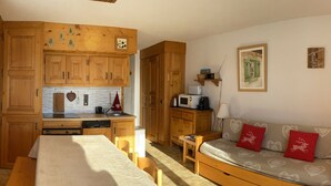 A compact living space with a kitchenette, a dining area, and a sofa with heart-patterned cushions.