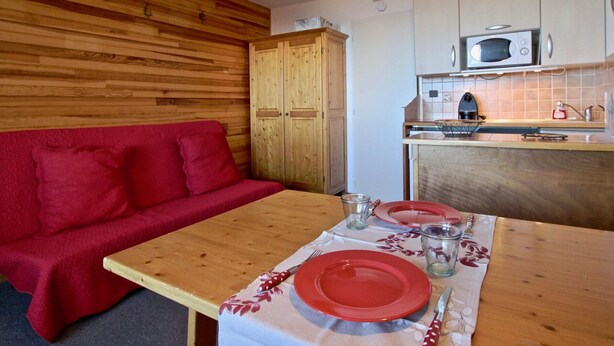 Cocina compacta con muebles de madera, microondas y un pequeño comedor con mesa para dos.
