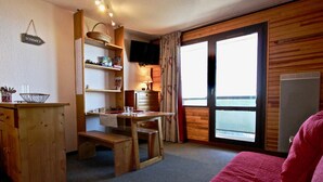 Una habitación acogedora con un escritorio de madera, una silla, una cama con una colcha roja, una ventana con vistas y un televisor en la pared.