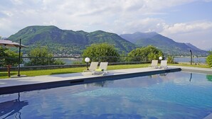 A swimming pool with two lounge chairs and a lamp post, surrounded by a fence and a view of mountains.