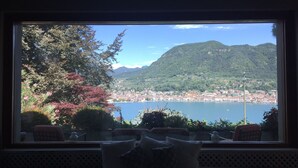 A view from a window with a bench, overlooking a lake and a town with mountains in the background.
