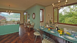 A dining area with a table set for four, surrounded by chairs, a chandelier, and a view of a lake and mountains.