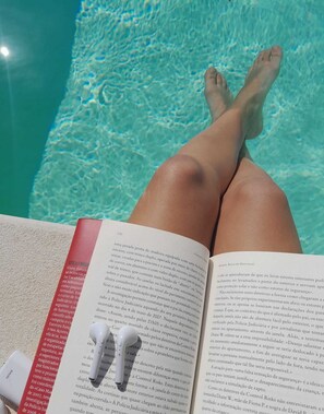 A person lying in a pool with legs extended, reading a book. - Feather House Home (São Bartolomeu de Galegos)