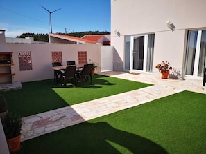 A modern outdoor patio with artificial grass, a stone pathway, and a dining area with chairs and a table.