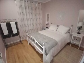 A bedroom with a bed, a bedside table, a lamp, a mirror, and a wardrobe.