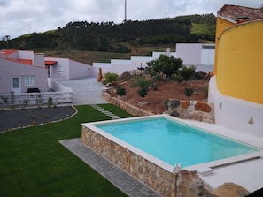 A swimming pool with a stone border, surrounded by a well-maintained lawn and a few trees. - Feather House Home (São Bartolomeu de Galegos)