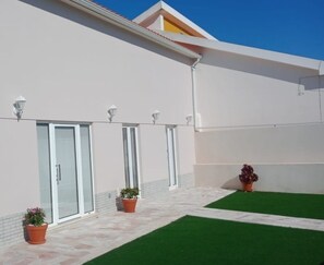 A modern building with a flat roof, large windows, and a paved patio area with artificial grass and potted plants. - Feather House Home (São Bartolomeu de Galegos)