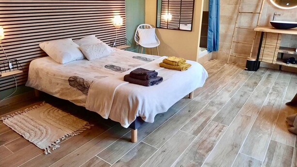 A neatly made bed with a white bedspread and pillows, a small round mirror above the bed, and a wooden floor. - Charming Cottage near Loire River with Garden, Covered Terrace & Easy Access to Saumur Attractions (Brain-sur-Allonnes)