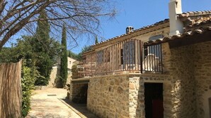 Um edifício de pedra com varanda, um caminho de pedra e uma árvore ao fundo.