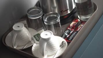 Sur une table, on trouve un plateau avec une cafetière, une bouteille d’eau, deux tasses et deux sachets de café instantané.