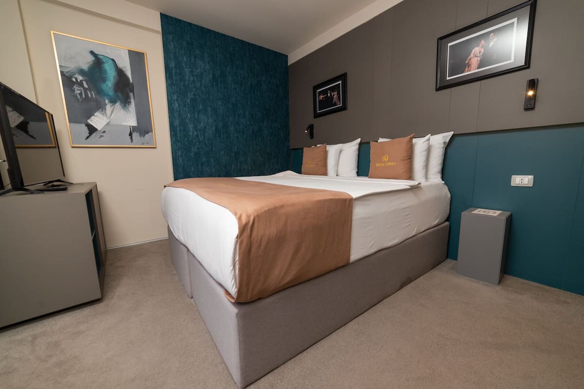 A modern hotel room with a large bed, a desk, and a wardrobe.
