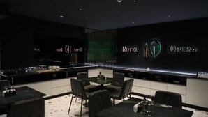 A modern hotel bar with a dark interior, a bar counter, and seating area with tables and chairs. - Hotel Opera (Pristina)