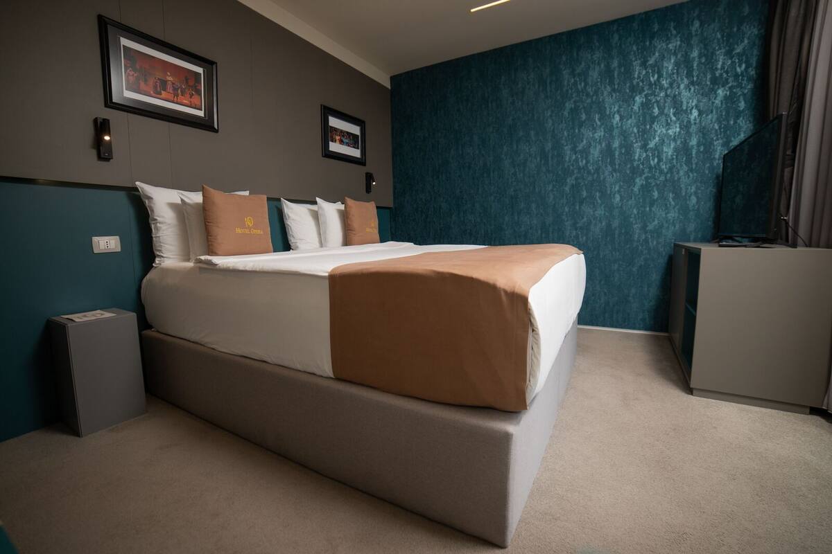 A hotel room with a large bed, a desk, and a blue textured wall.
