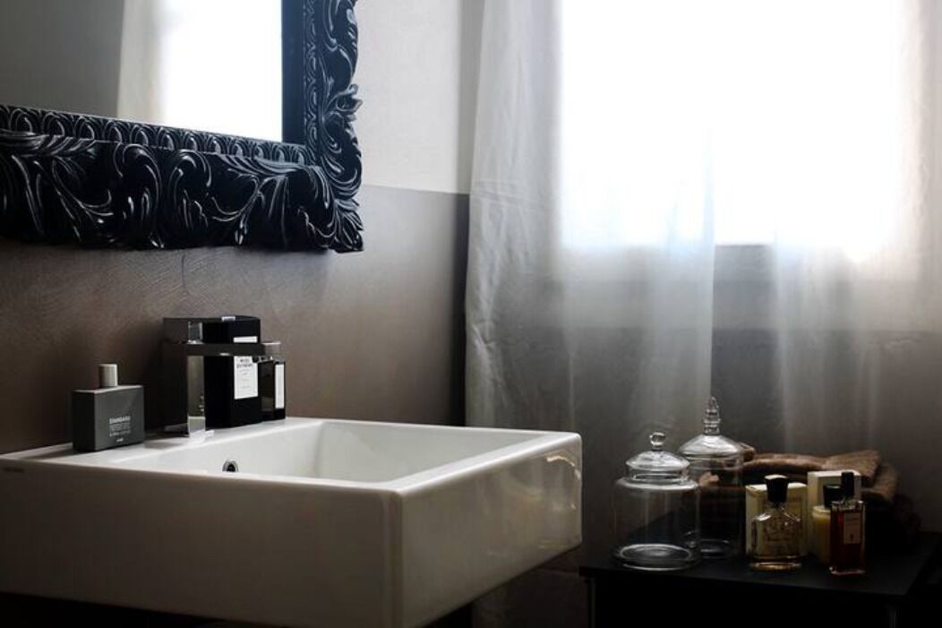 A bathroom with a large white sink, a mirror with a decorative frame, and a vanity table with toiletries.