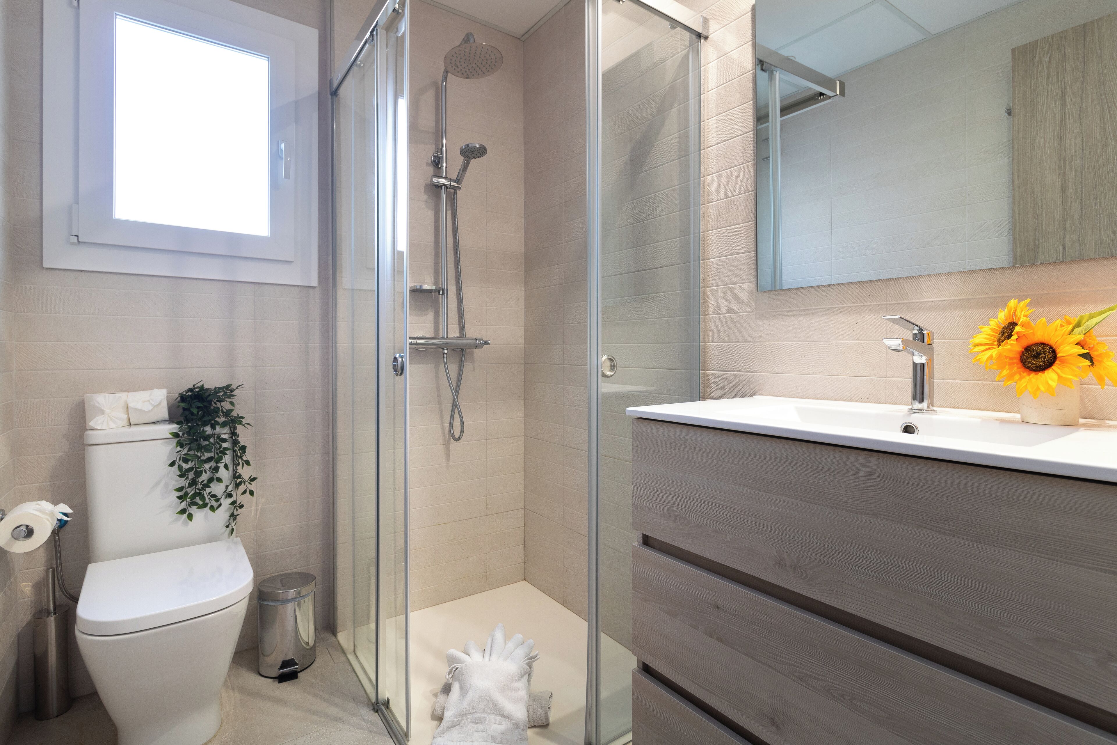 A modern bathroom with a glass shower enclosure, a toilet, a sink with a mirror, and a potted plant.