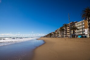 A beach with a row of multi-story buildings, palm trees, and a clear blue sky. - Calafell Home Apartments (Calafell)