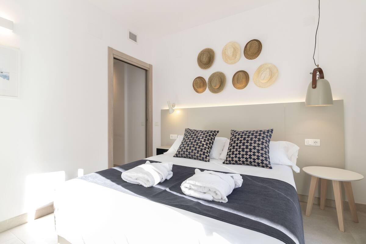 Una habitación de hotel moderna con una cama bien hecha, una mesita de noche y una lámpara de pared.