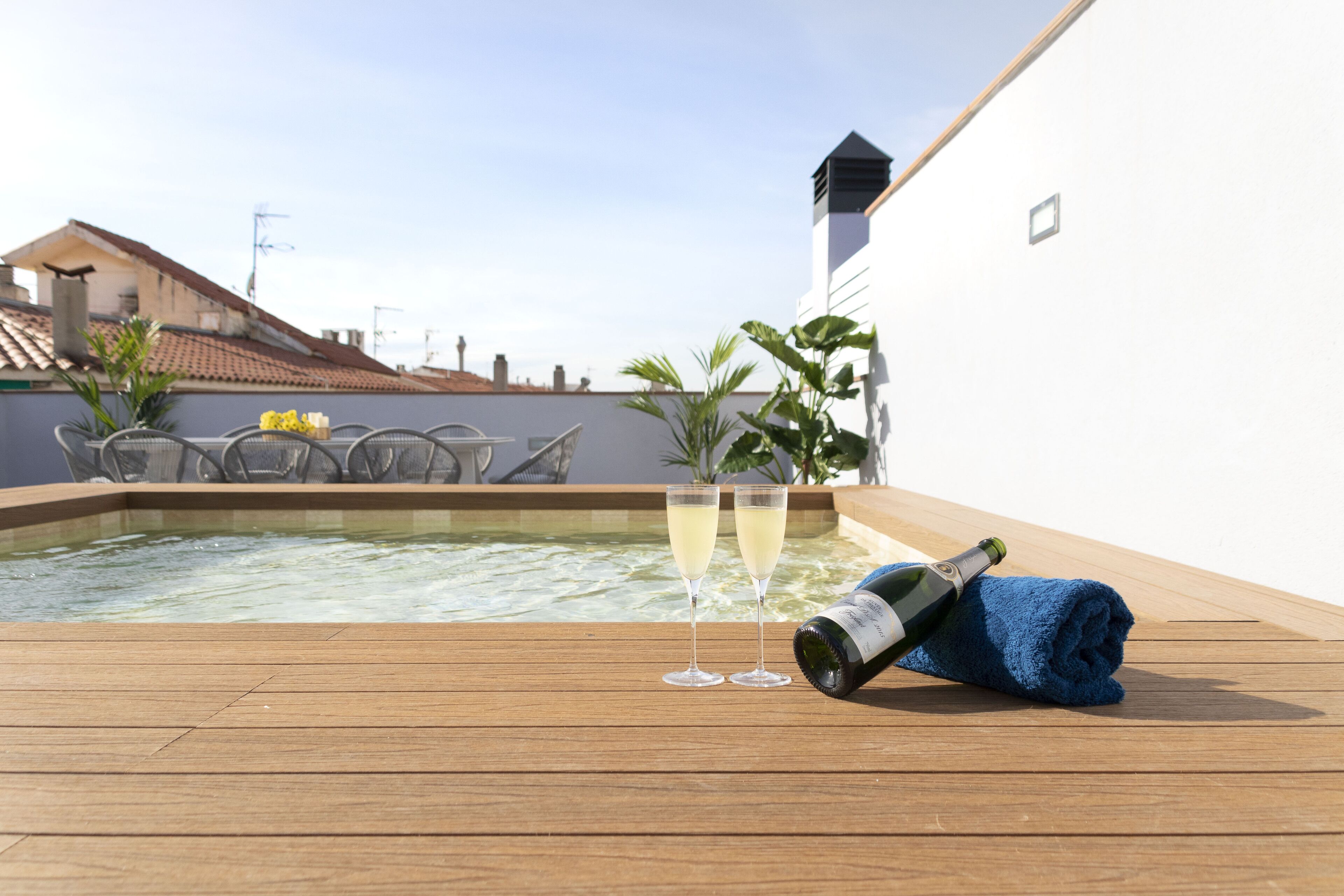 A wooden deck with a hot tub, two glasses of champagne, and a bottle on a towel.