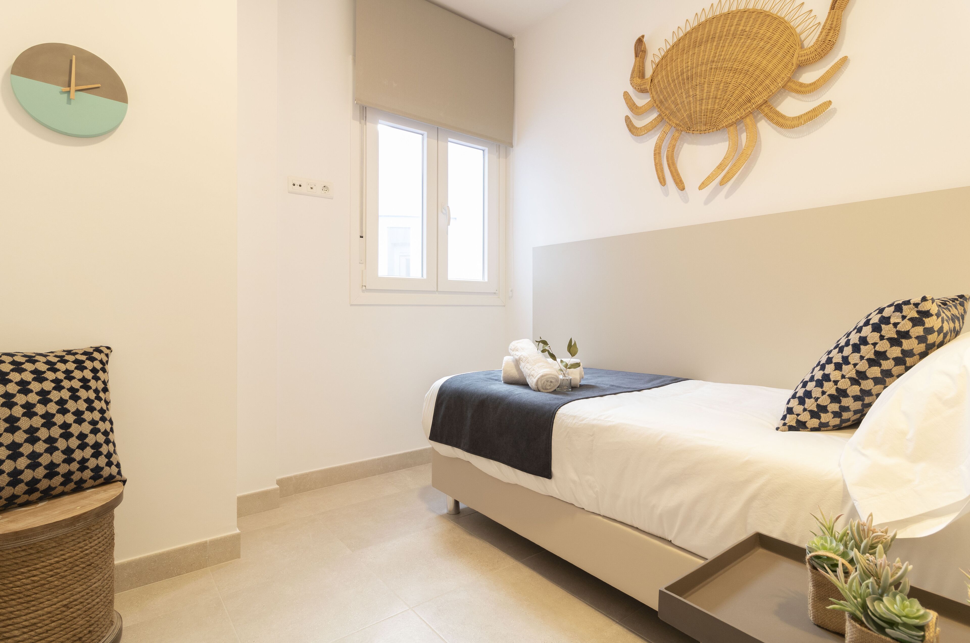 A bedroom with a bed, a wall clock, a window, and a decorative crab wall art piece.