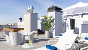 Une terrasse sur le toit avec des chaises longues blanches, une table avec une boisson et une plante en pot.