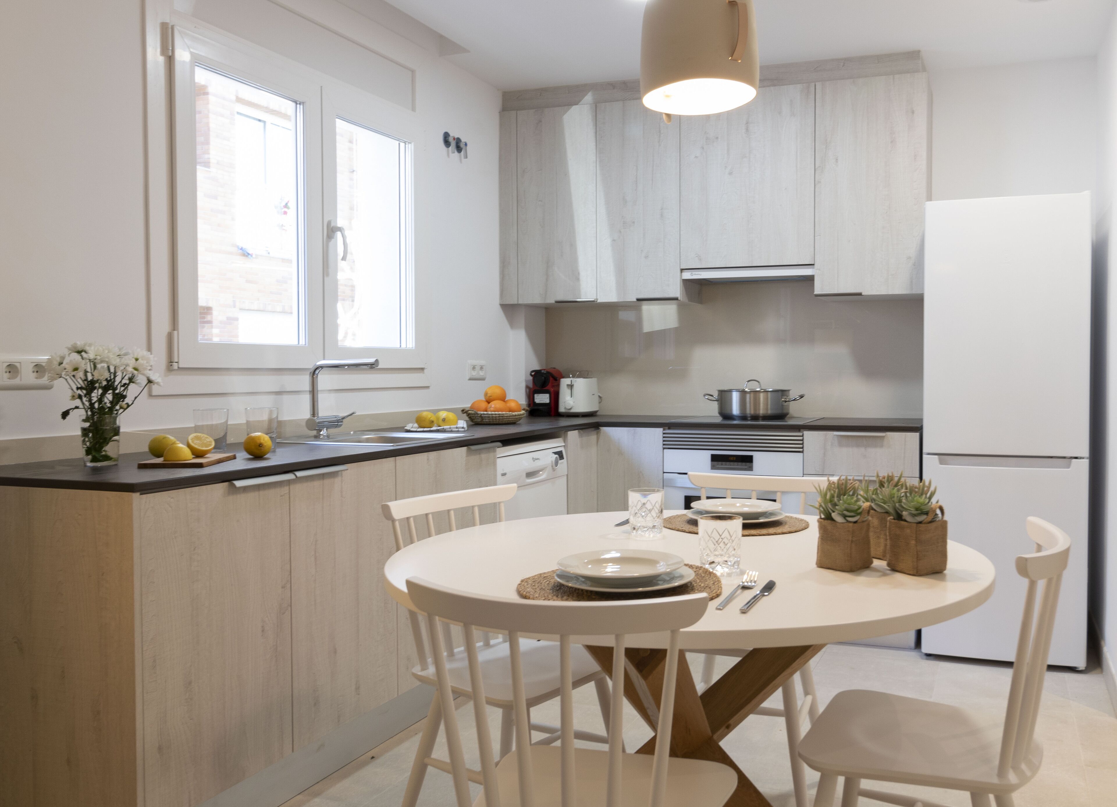 Et moderne køkken med en central ø, hvide skabe og et spiseområde med hvide stole.