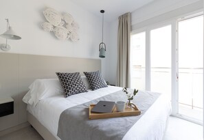 A modern bedroom with a bed, a tray with a laptop and mug, a hanging light, and a balcony view. - Calafell Home Apartments (Calafell)