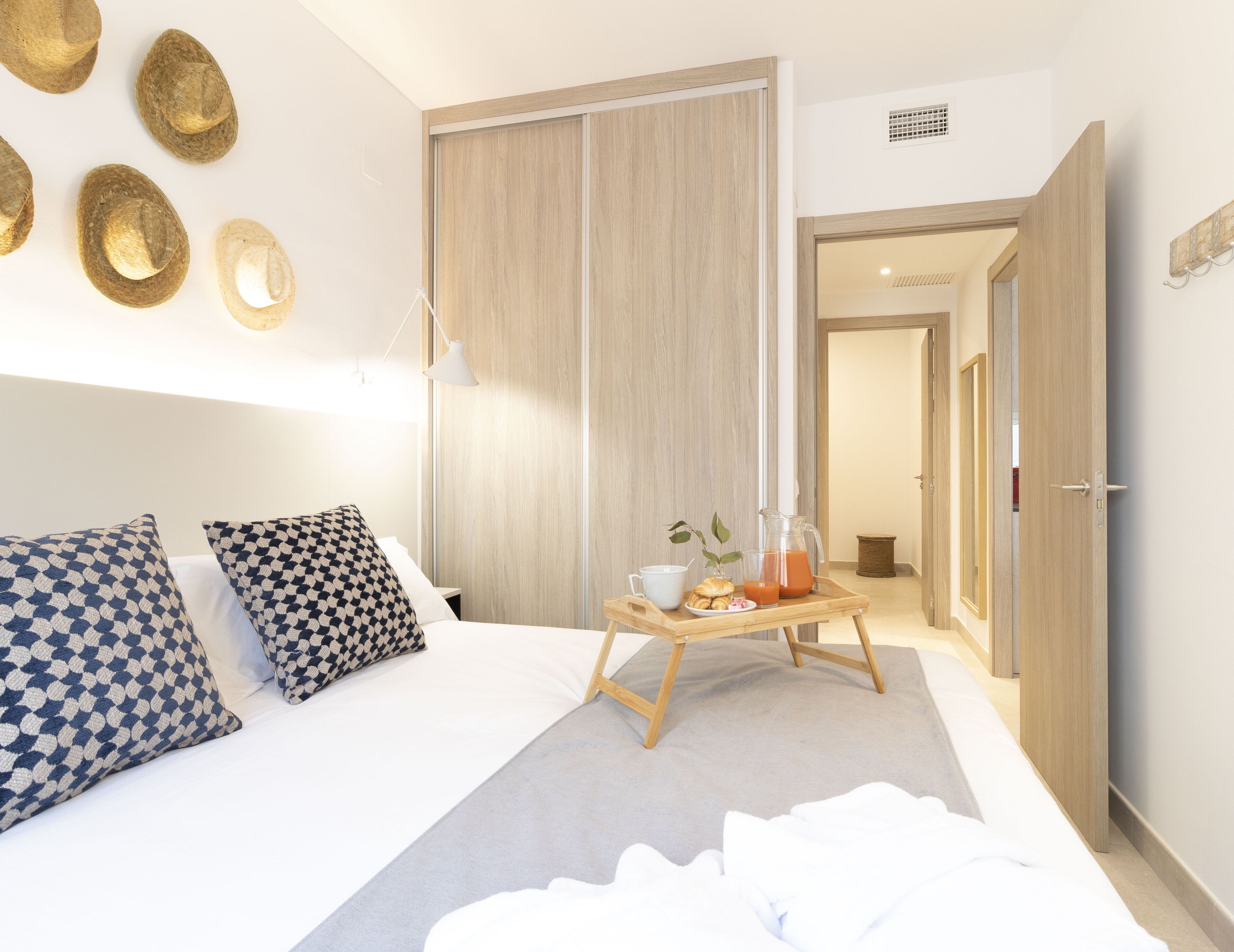 Een moderne hotelkamer met een groot bed, een nachtkastje met een ontbijtje erop, een kledingkast en uitzicht op de gang.