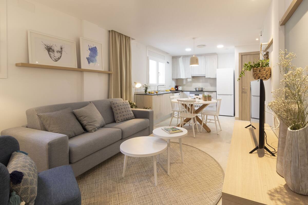 Una sala de estar moderna con un sofá gris, una mesa de centro redonda y una zona de comedor con una mesa y sillas blancas.
